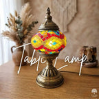 Colorful mosaic table lamp on a wooden surface with decorative elements in the background.
